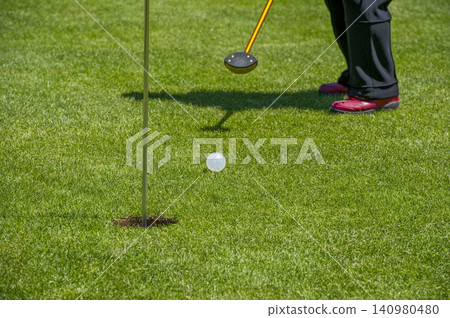 Playing golf on a green course, putting towards the hole in park golf. Playing golf on a green course, putting towards the hole in park golf. 140980480