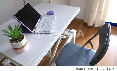Modern workspace featuring a purple laptop, mouse, and potted plant on a white desk with a gray folding chair in a well-lit room Modern workspace featuring a purple laptop, mouse, and potted plant on a white desk with a gray folding chair in a well-lit room 140981326