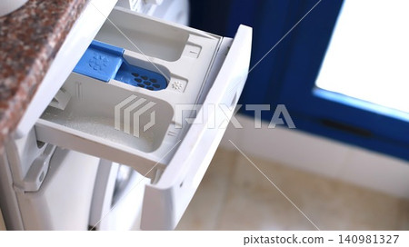 Close-up view of an open washing machine detergent drawer with blue compartment for fabric softener and white space for detergent in a bright laundry room Close-up view of an open washing machine detergent drawer with blue compartment for fabric softener and white space for detergent in a bright laundry room 140981327