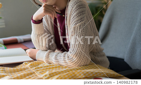 Young fashion designer in knit cardigan reviewing fabric swatches and sketches at cozy home studio workspace Young fashion designer in knit cardigan reviewing fabric swatches and sketches at cozy home studio workspace 140982178