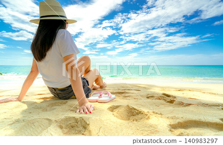 Back view of a female traveler relaxing alone on a quiet tropical beach with crystal clear sea and soft golden sand. Summer holiday, wellness retreat, tourism promotion, and mindful escape themes. Back view of a female traveler relaxing alone on a quiet tropical beach with crystal clear sea and soft golden sand. Summer holiday, wellness retreat, tourism promotion, and mindful escape themes. 140983297