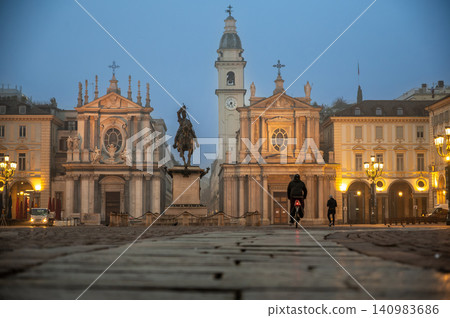 Turin, piedmont, italy. November 20, 2024. Cyclist and pedestrian crossing piazza san carlo in turin, italy, appreciating the architecture of the twin churches at dawn 140983686