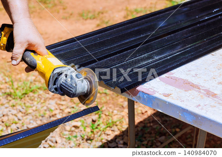 Carpenter operates cutting tool on metal sheets on table in construction outdoor area. Carpenter operates cutting tool on metal sheets on table in construction outdoor area. 140984070