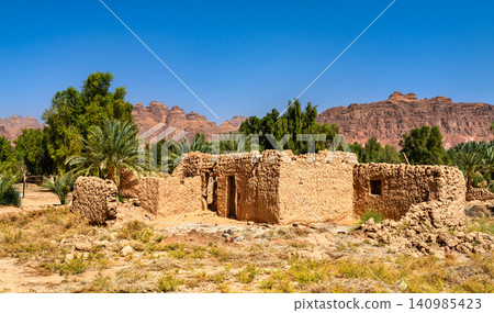 Ruins of ancient mud-brick houses surrounded by palm trees and sandstone mountains in AlUla Old Town, Saudi Arabia. Ruins of ancient mud-brick houses surrounded by palm trees and sandstone mountains in AlUla Old Town, Saudi Arabia. 140985423