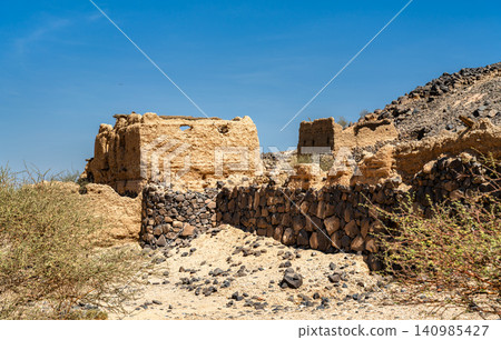 Traditional mud brick ruins and stone walls of Shanqal Fort under a clear blue sky in Saudi Arabia. Traditional mud brick ruins and stone walls of Shanqal Fort under a clear blue sky in Saudi Arabia. 140985427