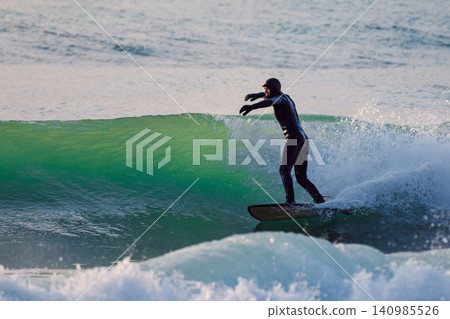 Surfer male rides and pumping on glassy wave in sea with evening sunlight Surfer male rides and pumping on glassy wave in sea with evening sunlight 140985526
