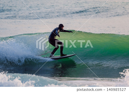 Surfer man rides on glassy wave in winter ocean with evening sun light Surfer man rides on glassy wave in winter ocean with evening sun light 140985527