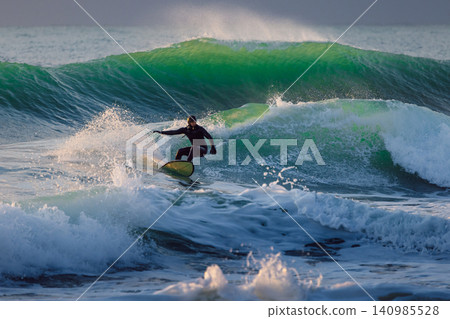 Surfer on wave in cold ocean. Winter surfing with evening sunlight Surfer on wave in cold ocean. Winter surfing with evening sunlight 140985528