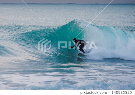 Surfer rides on wave in ocean. Winter cold surfing on waves Surfer rides on wave in ocean. Winter cold surfing on waves 140985530
