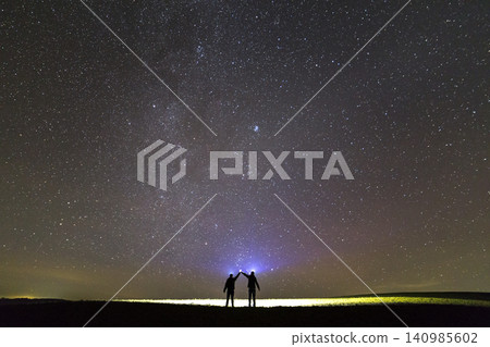 Back view of two men with head flashlights on green grassy field under dark blue summer starry sky. Back view of two men with head flashlights on green grassy field under dark blue summer starry sky. 140985602