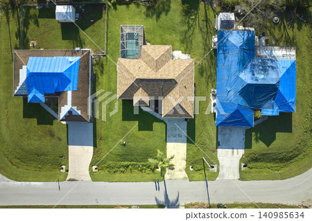 Hurricane Ian damaged house rooftop covered with protective plastic tarp against rain water leaking until replacement of asphalt shingles. Aftermath of natural disaster Hurricane Ian damaged house rooftop covered with protective plastic tarp against rain water leaking until replacement of asphalt shingles. Aftermath of natural disaster 140985634
