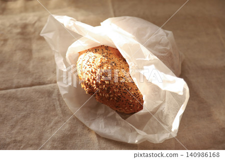 Seeded bread roll in white paper bag on linen cloth Seeded bread roll in white paper bag on linen cloth 140986168