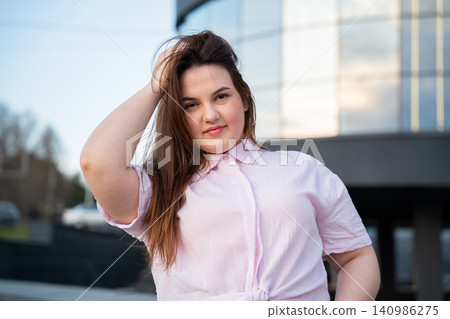 Confident young woman expressing individuality in front of sleek urban architecture. Casual outdoor portrait with contemporary urban lifestyle appeal Confident young woman expressing individuality in front of sleek urban architecture. Casual outdoor portrait with contemporary urban lifestyle appeal 140986275