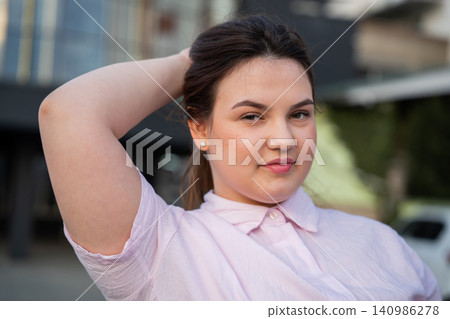 Confident young woman smiling with her hand holding her hair outdoors in an urban setting. Positive emotion and self-confidence in a casual portrait Confident young woman smiling with her hand holding her hair outdoors in an urban setting. Positive emotion and self-confidence in a casual portrait 140986278
