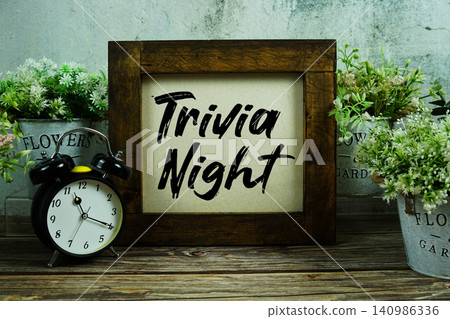Trivia Night text with alarm clock on wooden background Trivia Night text with alarm clock on wooden background 140986336