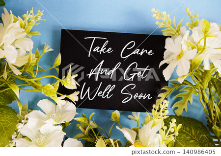 Take Care And Get Well Soon text written on paper card with flowers decoration on blue background Take Care And Get Well Soon text written on paper card with flowers decoration on blue background 140986405