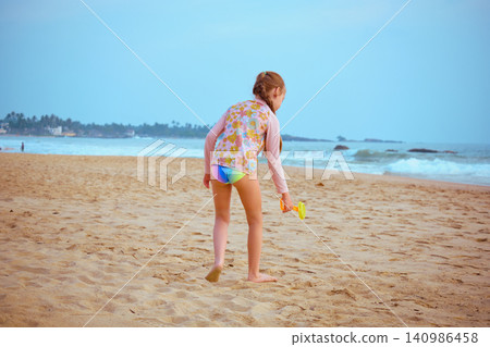 Little girl playing with yellow shovel on tropical beach Hikkaduwa Sri Lanka Little girl playing with yellow shovel on tropical beach Hikkaduwa Sri Lanka 140986458