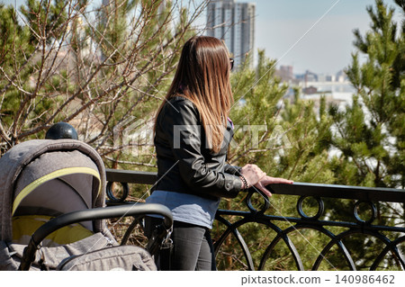 Urban park scene showing mother and child stroller overlooking city skyline Urban park scene showing mother and child stroller overlooking city skyline 140986462