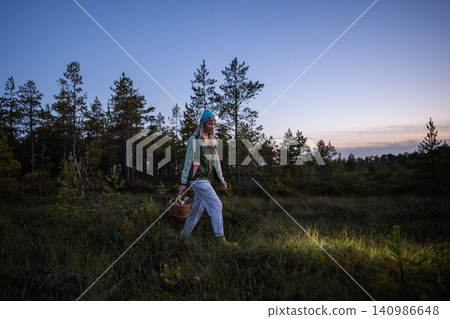 Woman walks in autumn swamp forest with basket mushrooms at dusk, lighting way with headlamp on head Woman walks in autumn swamp forest with basket mushrooms at dusk, lighting way with headlamp on head 140986648