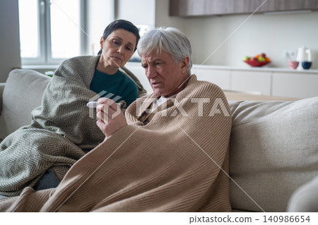 Exhausted elderly suffering from seasonal cold disease, husband checking temperature Exhausted elderly suffering from seasonal cold disease, husband checking temperature 140986654
