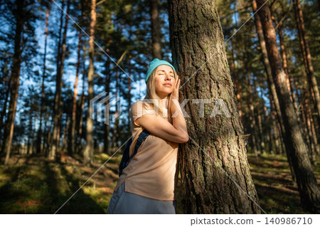 Relaxed woman touching tree trunk in forest, closed eyes and basking at sunlight. Stress free.  140986710