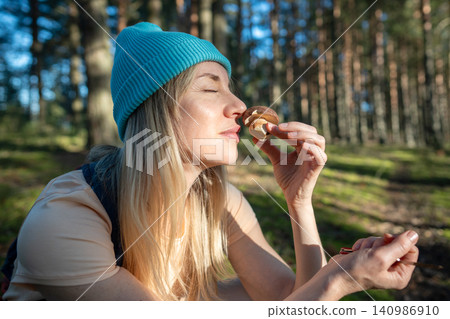 Woman forager holding boletus mushroom and smelling scent, picking porcini mushroom in autumn forest Woman forager holding boletus mushroom and smelling scent, picking porcini mushroom in autumn forest 140986910