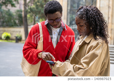Focused african american couple man and woman friends discussing and watching media on smartphone. Focused african american couple man and woman friends discussing and watching media on smartphone. 140987023