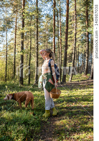 Active woman backpacker forager hunting in wild pine forest for edible mushrooms with domestic dog. Active woman backpacker forager hunting in wild pine forest for edible mushrooms with domestic dog. 140987038