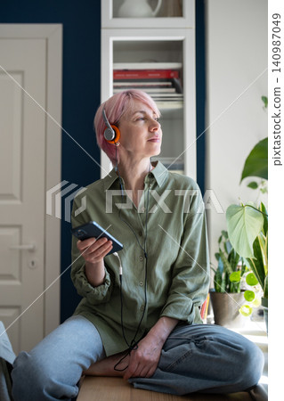 Relaxed mature woman using online music on-demand web streaming media platform on smartphone. 140987049