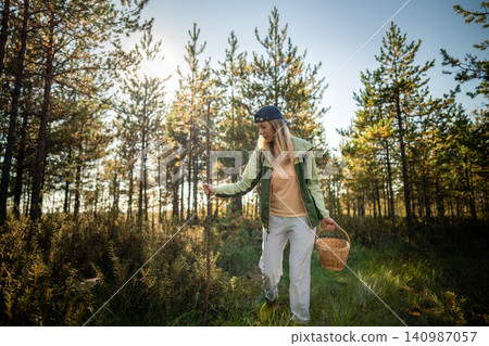 Woman mushroom hunter with basket and stick walks through wild woodlands searching for natural food Woman mushroom hunter with basket and stick walks through wild woodlands searching for natural food 140987057