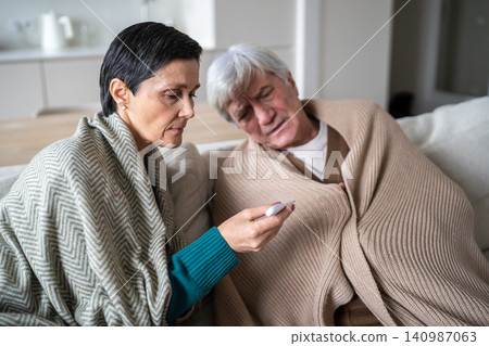 Tired unwell senior man woman on sofa under plaids, flu infection quarantine at home Tired unwell senior man woman on sofa under plaids, flu infection quarantine at home 140987063