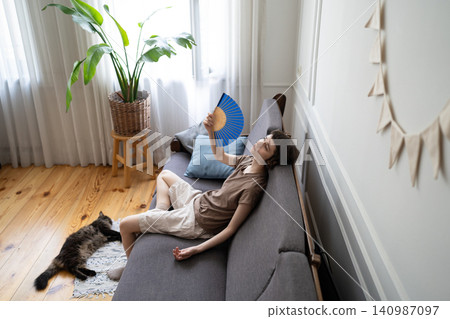 Suffering woman fanning, enduring high temperatures with pet struggling in airless apartment in heat Suffering woman fanning, enduring high temperatures with pet struggling in airless apartment in heat 140987097