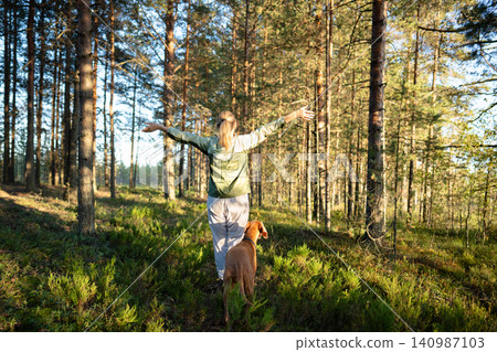 Happy woman nature lover enjoying recreation and healthy activity in forest together with Vizsla dog Happy woman nature lover enjoying recreation and healthy activity in forest together with Vizsla dog 140987103