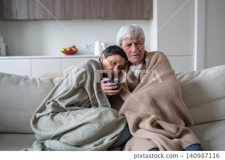 Upset senior man and woman covered in plaids sitting on sofa suffering from flu and weakness Upset senior man and woman covered in plaids sitting on sofa suffering from flu and weakness 140987116