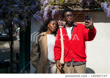 Stylish african american man and woman students pose for selfie outdoors on street together. Stylish african american man and woman students pose for selfie outdoors on street together. 140987147