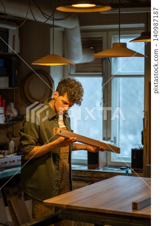 Serious focused male carpenter working preparing wooden block polishes removes dust with towel. Serious focused male carpenter working preparing wooden block polishes removes dust with towel. 140987187