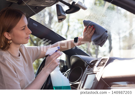 woman driver cleansing car windshield with spray, wipes with microfiber from dust and dirt.. 140987203