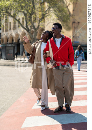 Carefree african american friends man and woman walk along crosswalk laughing and talking. Carefree african american friends man and woman walk along crosswalk laughing and talking. 140987348