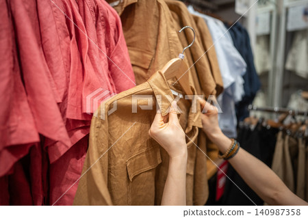 Woman customer shopping for clothes in fashion shop, choosing trendy outfit from new collection. Woman customer shopping for clothes in fashion shop, choosing trendy outfit from new collection. 140987358