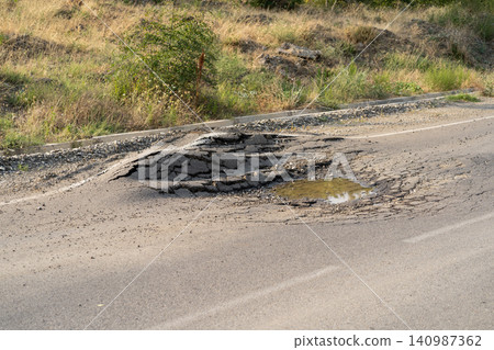 Deformed asphalt with potholes melts from heat due to heavy overloaded trucks driving at summer days Deformed asphalt with potholes melts from heat due to heavy overloaded trucks driving at summer days 140987362
