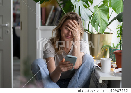 Confused woman doing facepalm gesture, looking at mobile phone, sent email to the wrong address Confused woman doing facepalm gesture, looking at mobile phone, sent email to the wrong address 140987382