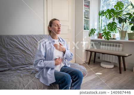 Positive mature woman practicing stress relief and deep breathing self helping therapy at home. Positive mature woman practicing stress relief and deep breathing self helping therapy at home. 140987446