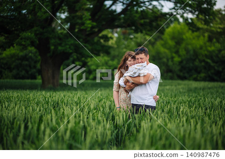 Smiling parents cradling newborn infant amid golden wheat, sunlight warming peaceful family moment Smiling parents cradling newborn infant amid golden wheat, sunlight warming peaceful family moment 140987476