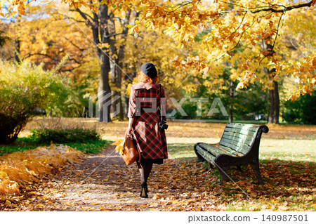 redhead woman in plaid coat and beret walks through the park at sunny day, back view. fall season redhead woman in plaid coat and beret walks through the park at sunny day, back view. fall season 140987501