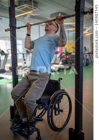 Man athlete in wheelchair doing vertical pull ups exercise using adaptive sports equipment at gym. Man athlete in wheelchair doing vertical pull ups exercise using adaptive sports equipment at gym. 140987545