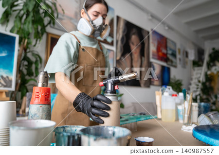 Concentrated craftswoman in protective respirator on face working with epoxy resin at home workshop. Concentrated craftswoman in protective respirator on face working with epoxy resin at home workshop. 140987557