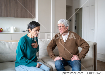 Elderly woman feeling sudden pain in heart while senior husband showing concern and support. Elderly woman feeling sudden pain in heart while senior husband showing concern and support. 140987623