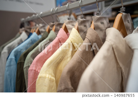 Colorful linen shirts hanging on hangers at clothing store, new collection on sale in showroom. Colorful linen shirts hanging on hangers at clothing store, new collection on sale in showroom. 140987655