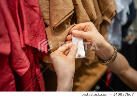 Woman client in trendy clothing store buying new shirt, checking tag with fabric content information Woman client in trendy clothing store buying new shirt, checking tag with fabric content information 140987667
