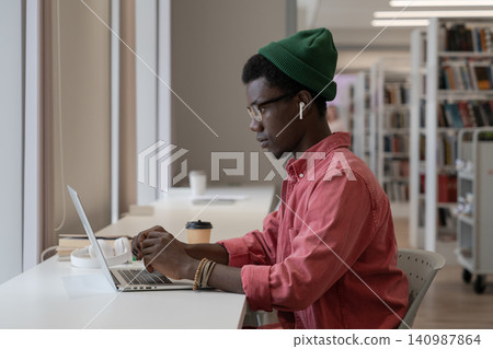 Pondered black intern man employee look at laptop screen typing text or browsing web for education. Pondered black intern man employee look at laptop screen typing text or browsing web for education. 140987864